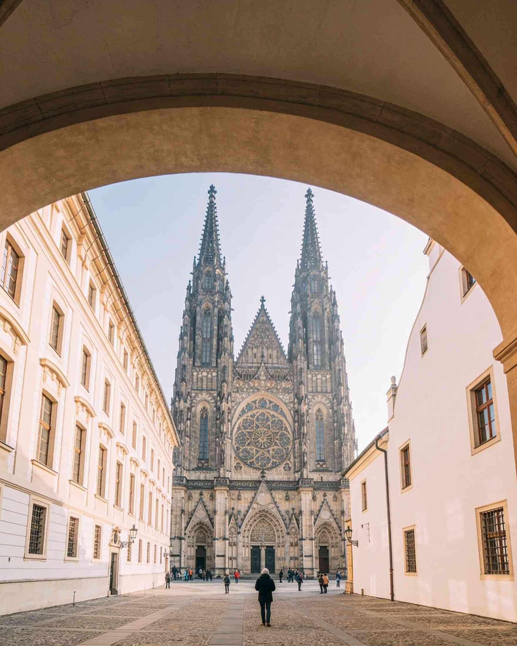 The Gothic west front of St Vitus Cathedral with its twin spires and rose window, seen through an archway in the castle