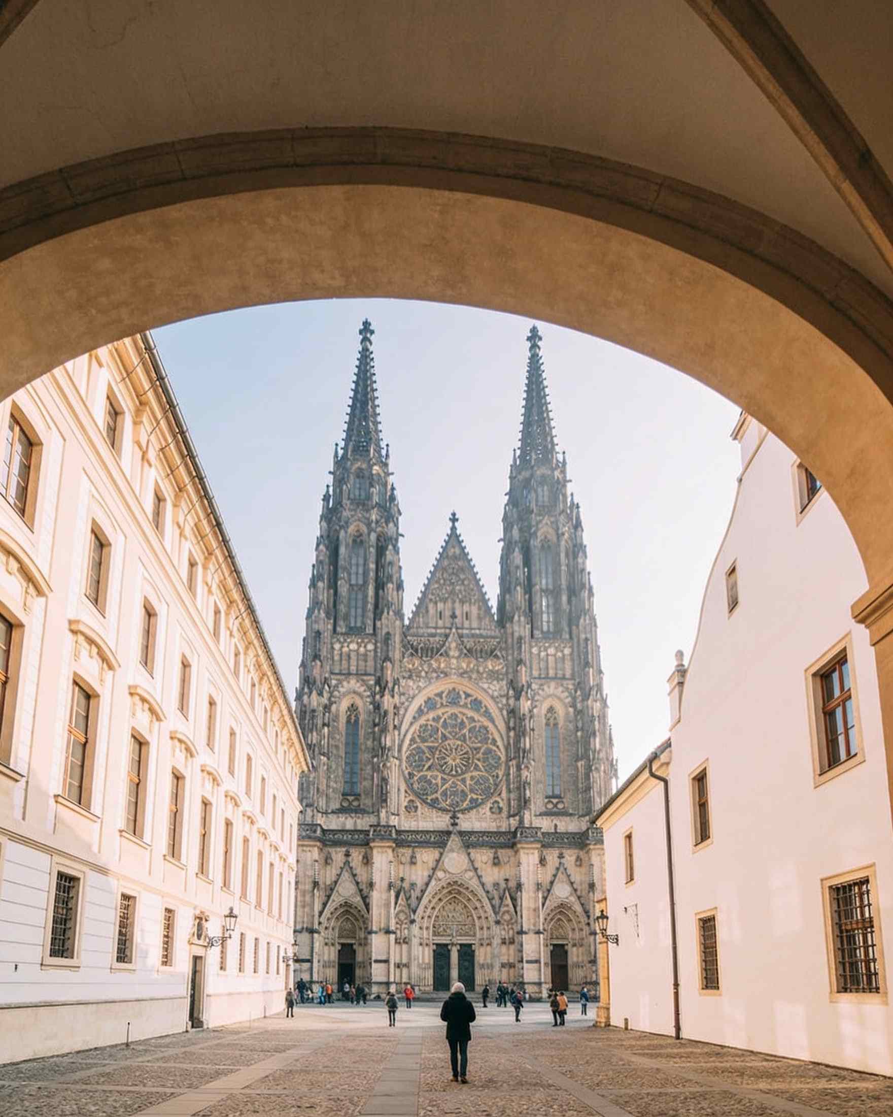 The Gothic west front of St Vitus Cathedral with its twin spires and rose window, seen through an archway in the castle